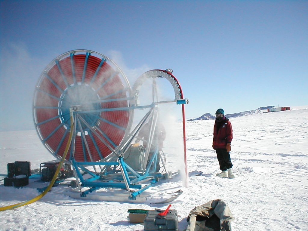 A man in a red jacket standing next to the shot hole drill